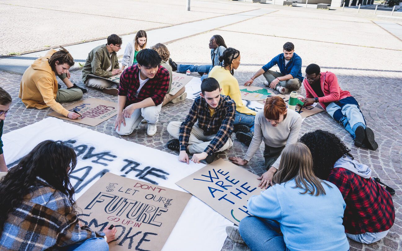 Large group of young girls and boys prepare to participate in a rally for environmental protection, activists draw signs with eco-themed slogans